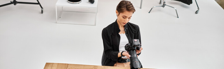 thoughtful young professional female photographer in casual attire holding modern camera, banner - obrazy, fototapety, plakaty