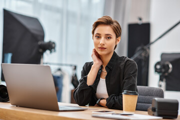 young beautiful woman in casual attire sitting at desk in her photo studio and looking at camera