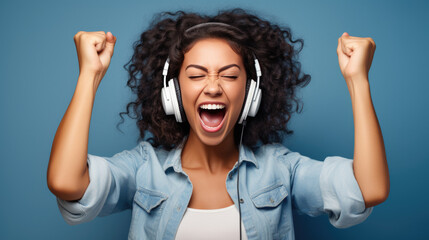 Woman with headphones on, her fists raised in excitement or victory, with a powerful expression of triumph or elation on her face against a blue background.
