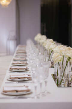 Sophisticated wedding reception table, featuring a linear arrangement of white roses and crystal glassware set against a soft-focused backdrop.