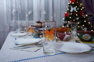 There are glasses and plates with food on the festive Christmas table. On the background of a decorated Christmas tree.
