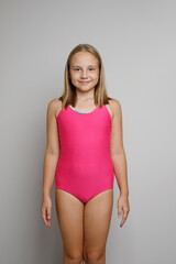 Pretty young girl in pink swimsuit posing on light gray studio wall background. Travel, sport,...