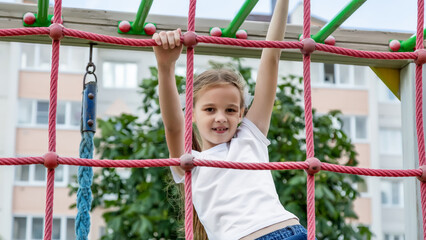 Obraz premium A child climbs up an alpine grid in a park on a playground on summer day. children's playground in a public park, entertainment and recreation for children