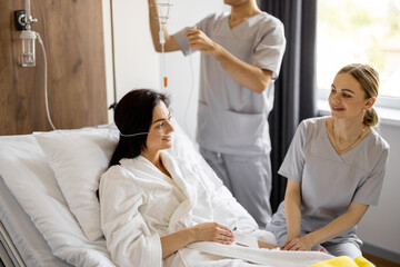 Nurse has a conversation with female patient lying in bed during rehabilitation or medical...