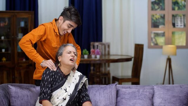 A loving grandson is giving a shoulder massage to his elderly grandmother - old age  exhaustion  tiredness  old age problems. Woman facing shoulder pain - home massage  muscle relaxation  stiff mus...