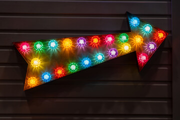 Illuminated Arrow Sign with colored Bulbs Mounted to a Brown Wooden Slat Wall