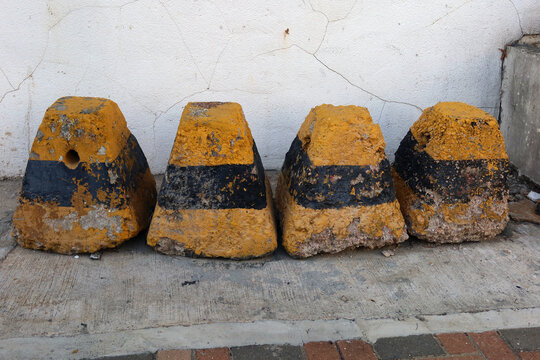 four old aged triangular pyramid shape yellow and black road rock cement warning alert blocks on the side of pavement