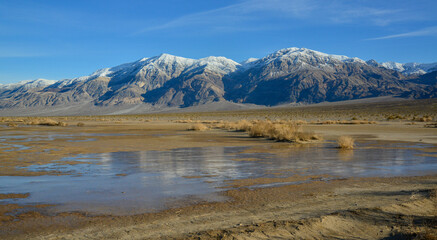 Landscape of wet clay desert in winter against the backdrop of snow-capped mountains in the Death Valley area