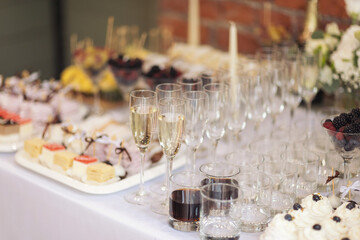 Party and holiday celebration concept. Many glasses of champagne on the table in the restaurant. Catering on wedding. Delicious fruits appetizers, desserts on stand, drinks, modern tab. 