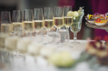 Party and holiday celebration concept. Many glasses of champagne on the table in the restaurant. Catering on wedding. Delicious fruits appetizers, desserts on stand, drinks, modern tab. 