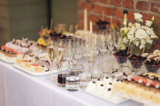 Party and holiday celebration concept. Many glasses of champagne on the table in the restaurant. Catering on wedding. Delicious fruits appetizers, desserts on stand, drinks, modern tab. 