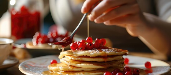 Girl or woman's hands eating healthy, low-cal fresh pancakes with red berry, jam, and coffee in...