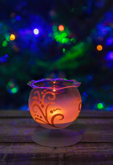 Glass candle light decoration on wood table with blured christmas tree on background