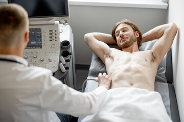 Young guy during an ultrasound diagnosis of the lower abdomen. The concept of ultrasound diagnostics and men's health - obrazy, fototapety, plakaty