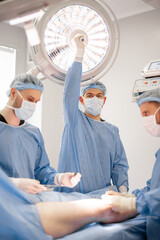 Three confident surgeons performing surgical operation on a patient's knee in operating room....