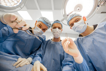 Portrait of three scary surgeons with a surgical tools look at camera in operating room