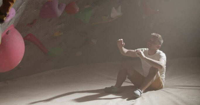 Young male climbing wall and sitting gym trainer