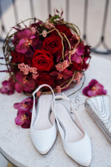 White high-heeled shoes stand near a wedding bouquet on the table
