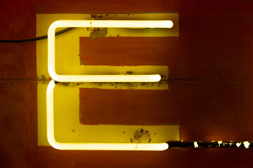 Obraz premium Neon yellow E letter illuminated on a sign at night