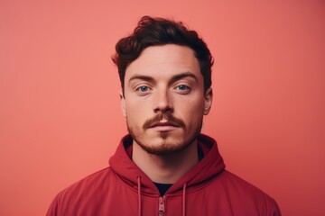 Portrait of a handsome young man in red hoodie looking at camera isolated over red background