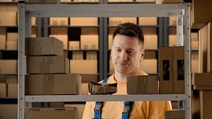 Portrait of male working in storage. Man storekeeper near rack checking packages with paper...