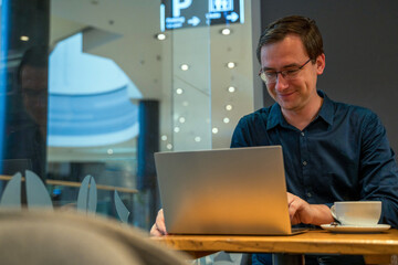 A man in shirt working on laptop inside a cafe with a coffee, business man working remotely concept
