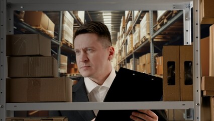 Portrait of storekeeper working in storage. Man manager in formal outfit standing near rack with...