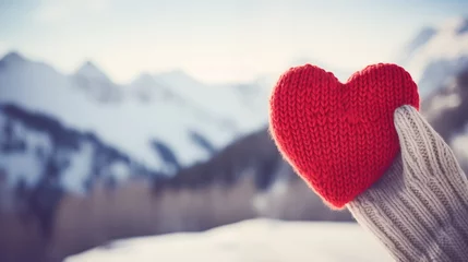 Rolgordijnen A red knitted heart in a hand with a snowy mountain landscape in the background. Valentine's Day, love, romance, winter, skiing and snowboarding, travel concept. Valentine's Day background. © Milan