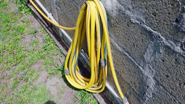 Yellow twisted long hose hanging on external wall, pipes for pump and irrigation system, industrial watering equipment