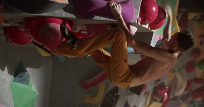 Young man climbing wall with help of holds