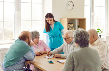 Friendly young nurse woman having conversation with a group of senior people men and women sitting...