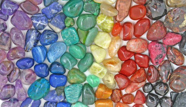 Chakra Crystal Healing Background - Rows of tumbled polished healing crystal laid out in chakra colours purple, indigo, turquoise blue, green, yellow, orange, red ideal for crystal healing theme
