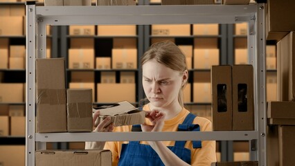 Portrait of female model working in storage. Girl storekeeper in uniform standing near rack with...