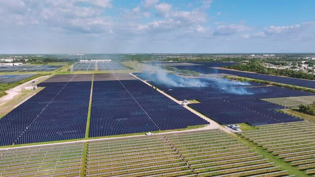 Dangerous wild fire at sustainable electric power plant with many rows of solar photovoltaic panels for producing clean electrical energy