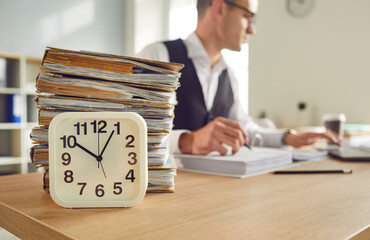 Overworked tired business man accountant working in office sitting at the desk with a clock and a...