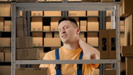 Portrait of male working in storage. Man storekeeper standing near rack with boxes tired face massaging neck has back pain after work.
