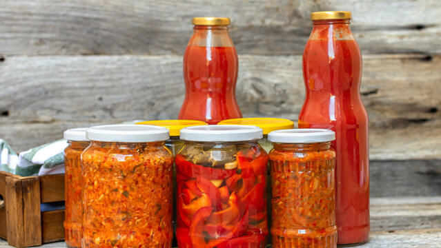 Glass jars with pickled red bell peppers and pickled cucumbers (pickles) isolated. Jars with variety of pickled vegetables, jars with zacusca and bottles with tomatoes sauce. Preserved food concept.