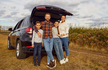 Full length portrait of family beside vehicle, embracing the joy of car travel. With children in tow, they embark on a leisure vacation, creating precious memories on the autumn road at nature.