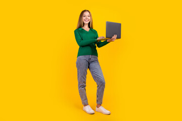 Photo of young smiling cheerful brown teen hair girl wear green jumper use laptop develop her web app isolated on yellow color background