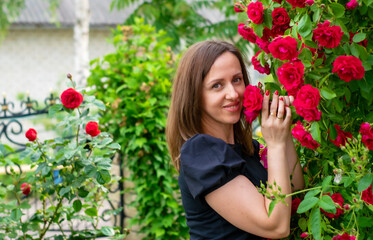A beautiful woman in a garden admires a fragrant bush of red roses.