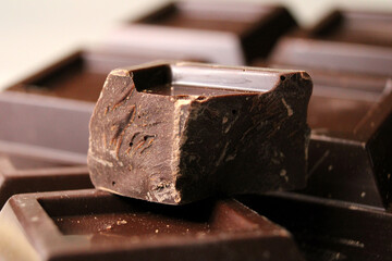 Piece of extra dark bitter chocolate on the background of a chocolate bar, used in confectionery. Close up view.