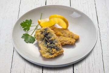 Batter-fried blue sardine fish with parsley leaves and lemon slices in a dish on white wooden table with clipping path included