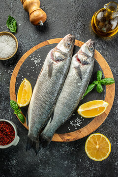 raw fish sea bass with ingredients on a dark background. vertical image. top view. place for text