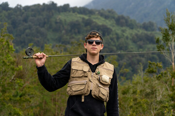 Fototapeta premium Young man with fishing gear and rod looking at camera