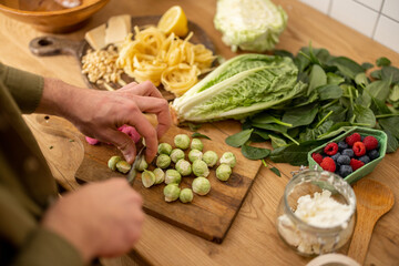 Man cutting brussels sprouts on cutting board cooking vegetarian pasta, close-up