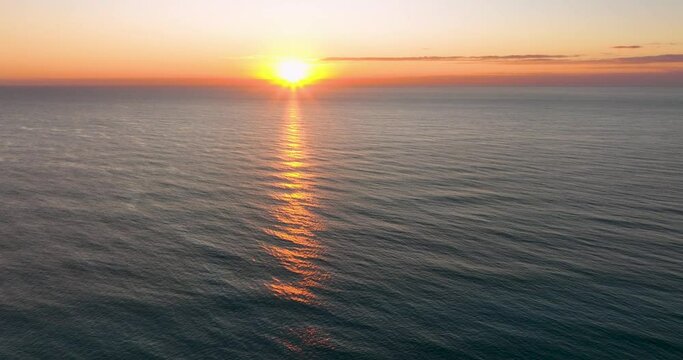 Aerial view of the ocean at sunrise with the sun casting a golden path on the water.