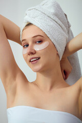 A woman with eye patches and a white towel looks sweetly at the camera