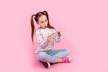 Foto op Canvas Full size photo of impressed schoolgirl dressed dotted pullover sit play in video game on smartphone isolated on pink color background © deagreez