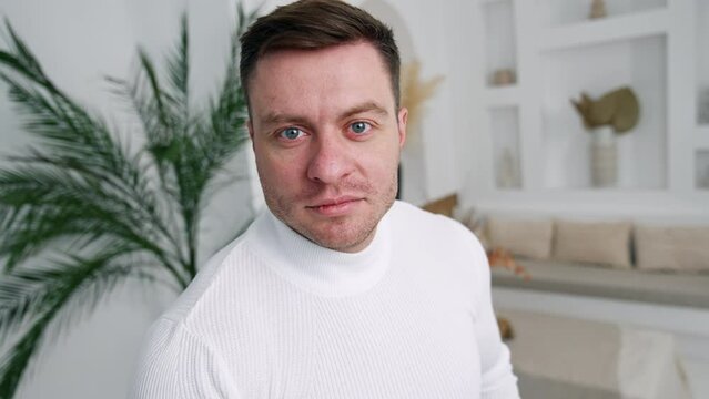 Caucasian male wearing white sweater standing near the camera. Cropped image of a man in the room. Close up.