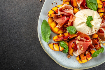 Heathy summer salad with grilled peach, ham and burrata on a dark background. top view. copy space for text - obrazy, fototapety, plakaty